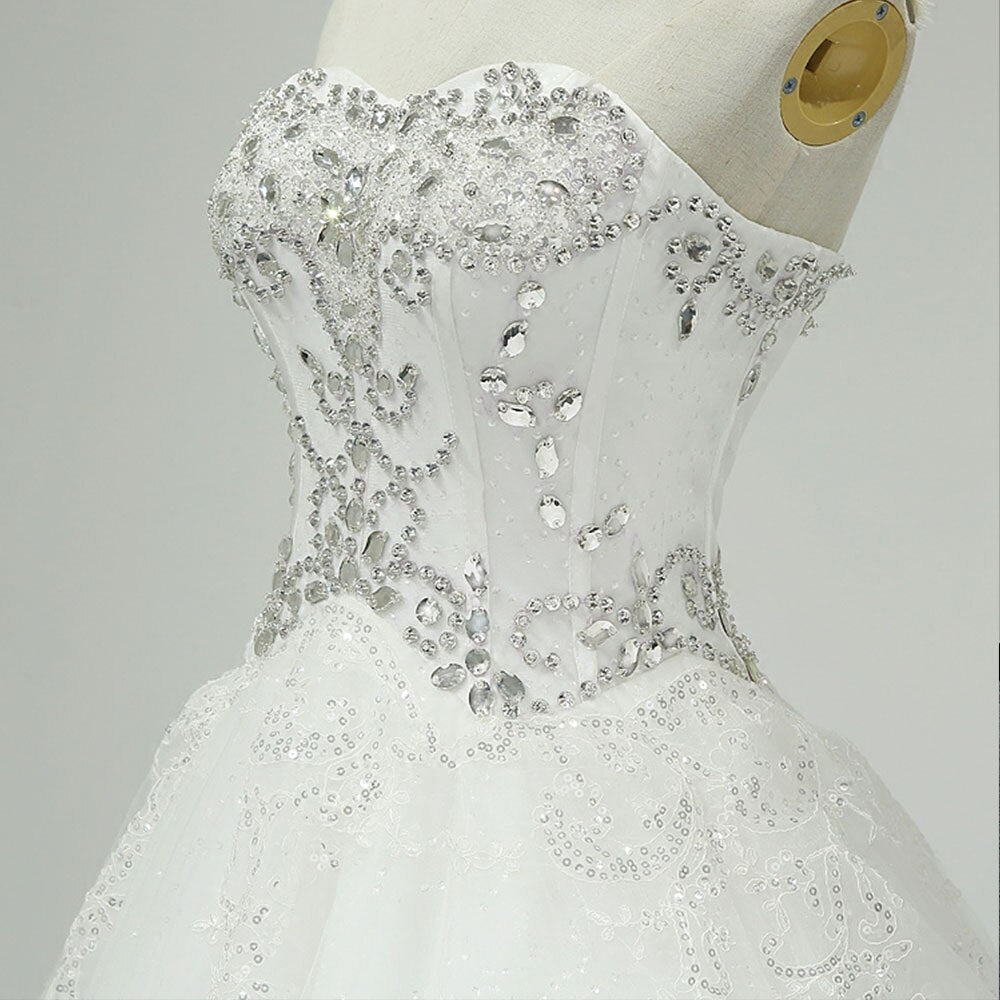 Close-up detail of the bodice of a wedding dress, highlighting the elaborate silver crystal beading and shimmering sequin work on a white fabric base.