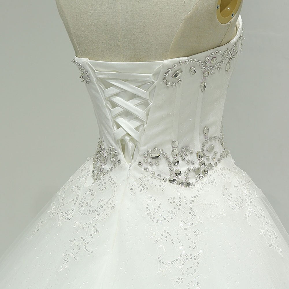 A detailed shot of the back of a strapless wedding gown featuring a lace-up corset closure surrounded by intricate crystal beading and sequins.