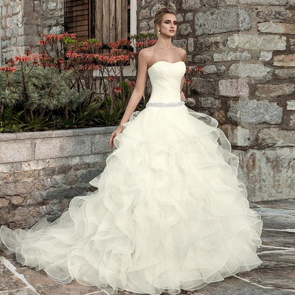 Front-facing shot of a strapless wedding ball gown with a clean pleated bodice and a shimmering crystal-beaded waist, emphasizing the luxury design.