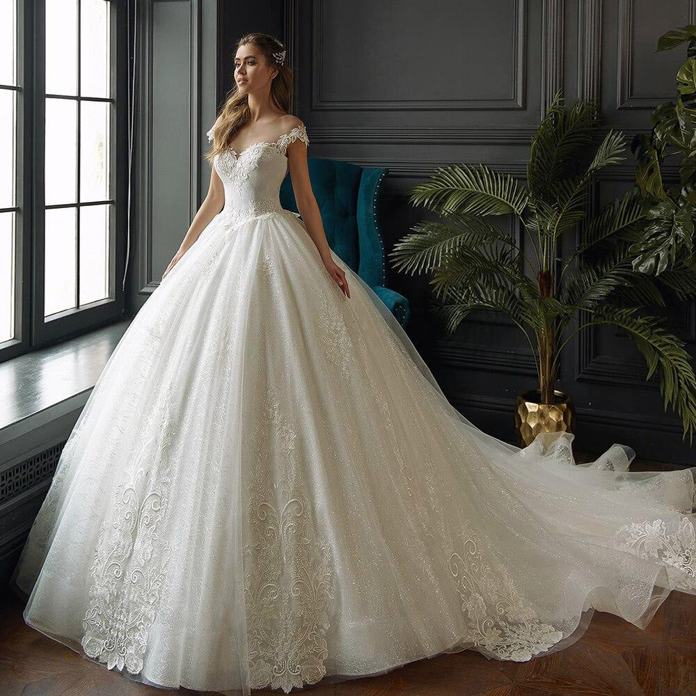 Elegant bride wearing a sparkling princess ball gown wedding dress with off-the-shoulder lace detailing.