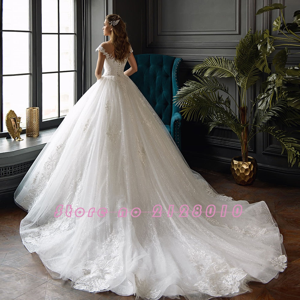 Full view of a bride wearing a voluminous, sparkling princess ball gown wedding dress with an extended train.