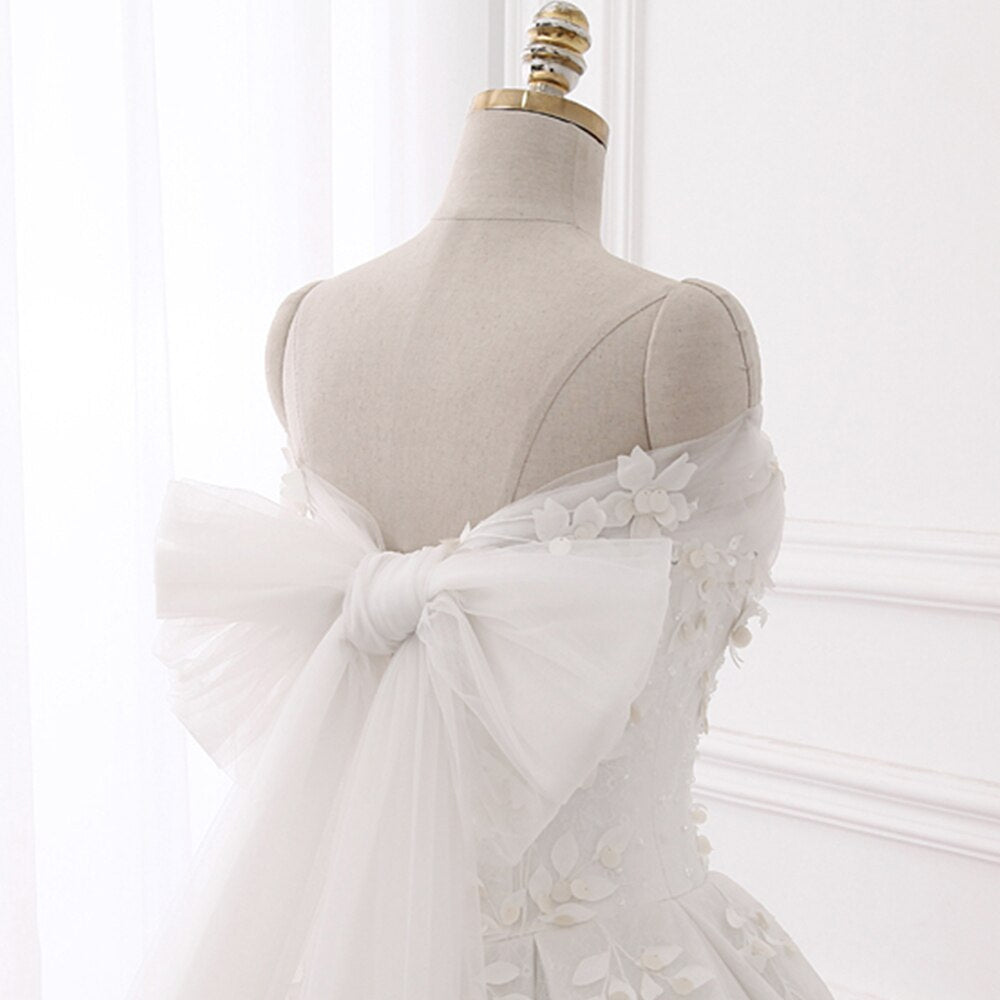 Back view of a princess ball gown wedding dress on a mannequin featuring a large tulle bow detail and a flowing train.