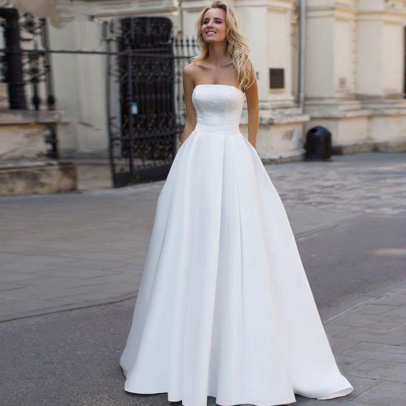 A beautiful bride wearing a classic strapless satin A-line wedding dress with a pearl-embellished bodice, captured in an outdoor urban setting.
