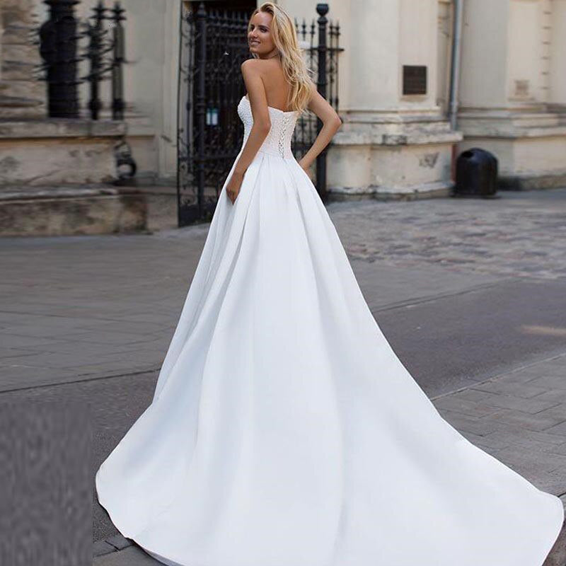 Rear view of an elegant satin A-line bridal gown featuring a strapless design, a lace-up back, and a long sweeping train.