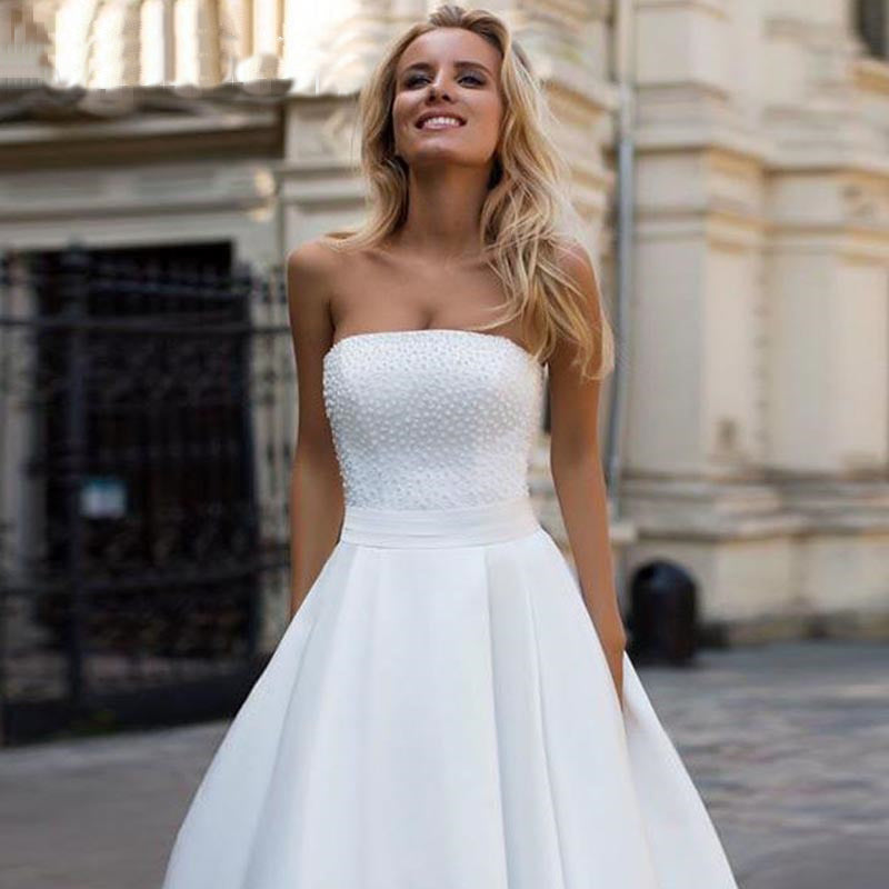 A close-up front portrait of a smiling bride in a strapless satin wedding dress with a beaded, pearl-detailed bodice.
