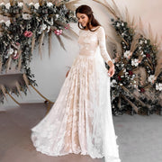 A bride wearing a sexy backless long-sleeve wedding dress with floral lace detailing, standing in front of a floral installation.