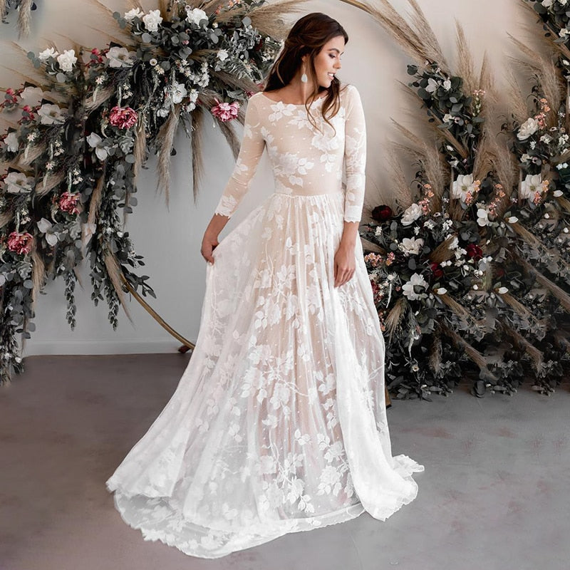 A bride smiling while posing in a romantic long-sleeve lace A-line bridal gown, perfect for a bohemian-style wedding.
