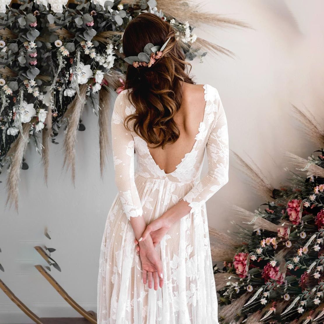 A bride standing in a backless long-sleeve lace wedding dress in front of a decorative floral circle arch.