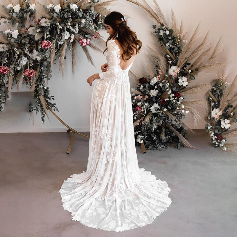 A bride looking down, smiling while wearing a long-sleeve floral lace wedding dress with an A-line skirt.