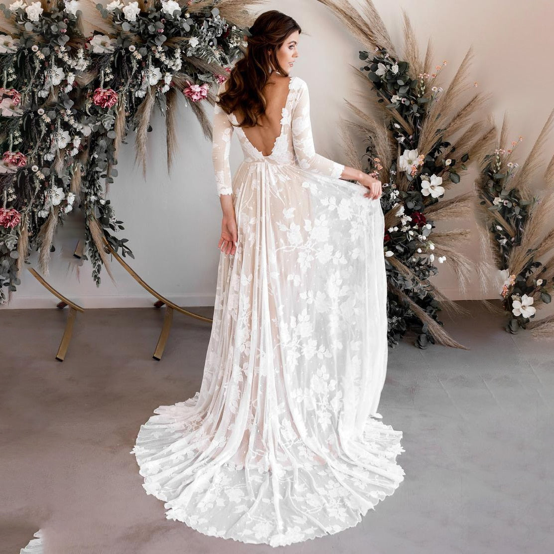 A beautiful bride standing and gracefully holding the skirt of her long-sleeve lace wedding dress