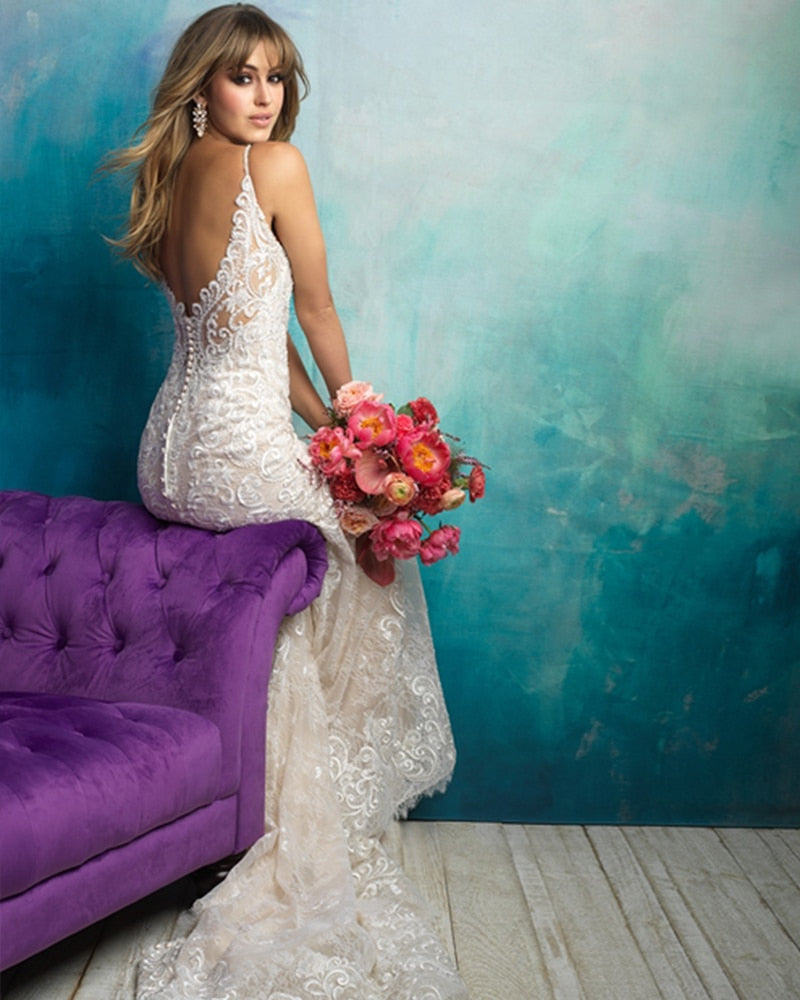 Back view of a bride sitting on a purple tufted sofa, showcasing the backless design of a mermaid wedding dress with a floral bouquet.