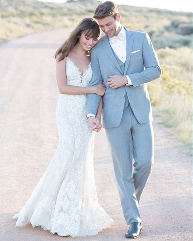 Romantic shot of a bride in a beaded mermaid wedding dress walking outdoors with a groom in a light grey suit.