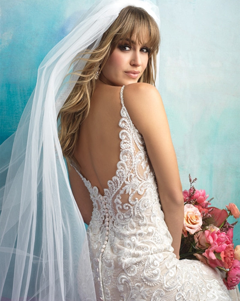 Romantic shot of a bride in a beaded mermaid wedding dress walking outdoors with a groom in a light grey suit.
