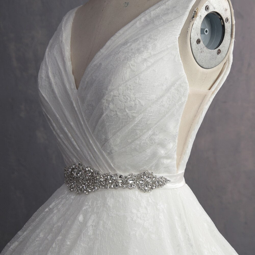 Detailed close-up of the intricate crystal-beaded belt on the waist of a V-neck ivory lace wedding gown.